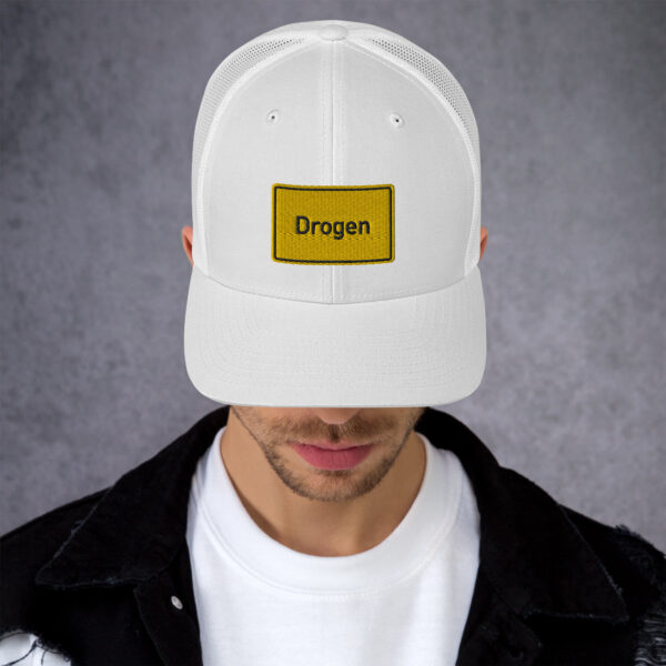 Ein Mann, der eine weiße Trucker-Mütze mit dem Drogen Trucker-Cap-Logo trägt.