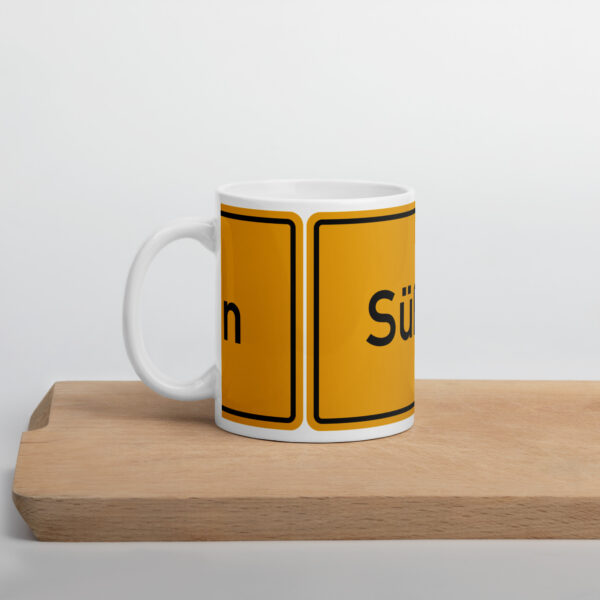 Eine glänzende Süßen - Weiße Tasse mit einem gelb-schwarzen Schild darauf.