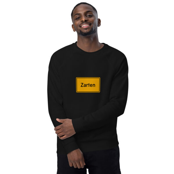 Ein Mann trägt einen schwarzen Unisex-Bio-Raglan-Pullover mit einem gelben Kästchen darauf.