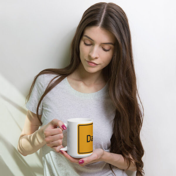 Eine Frau hält eine weiße, glänzende Tasse mit der Aufschrift „be“ in der Hand.